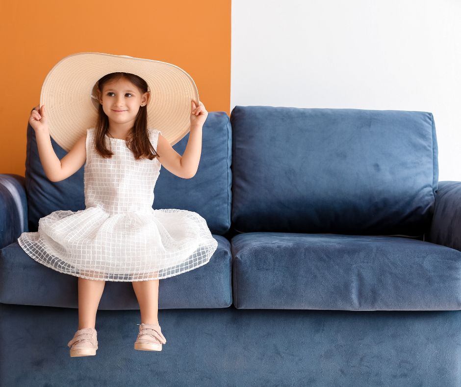 A wall painted half orange half white in the background where little girl smiling sitting on a sofa.